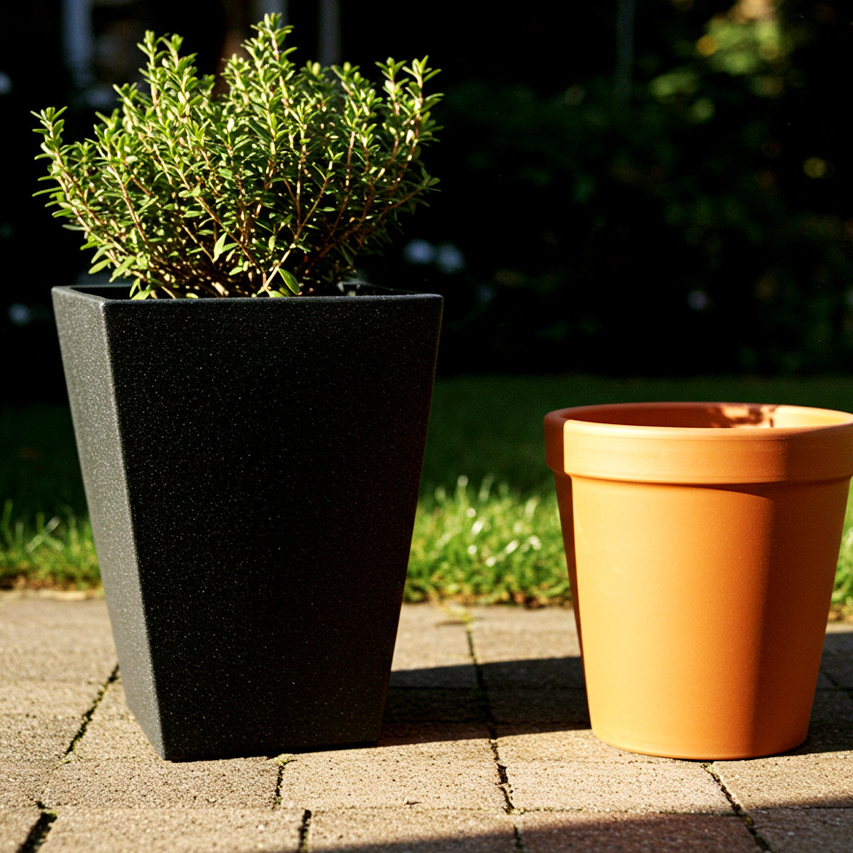 Fiberglass Planters Versus Other Planter Materials 3 A matte black fiberglass planter and a classic orange terracotta pot sit side by side on a sunlit patio, highlighting the difference in texture, color, and modern vs. traditional planter aesthetics.
