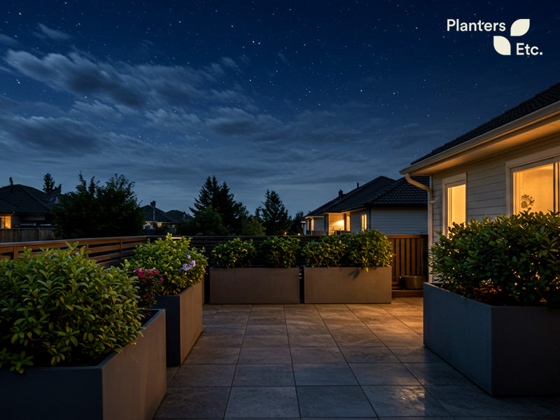 A tranquil nighttime patio scene featuring large, modern rectangular planters filled with lush greenery. Under a starry sky, the strategically placed planters not only enhance the aesthetics but also provide subtle sound deflection, creating a quiet, private outdoor space with warm ambient lighting from nearby homes.