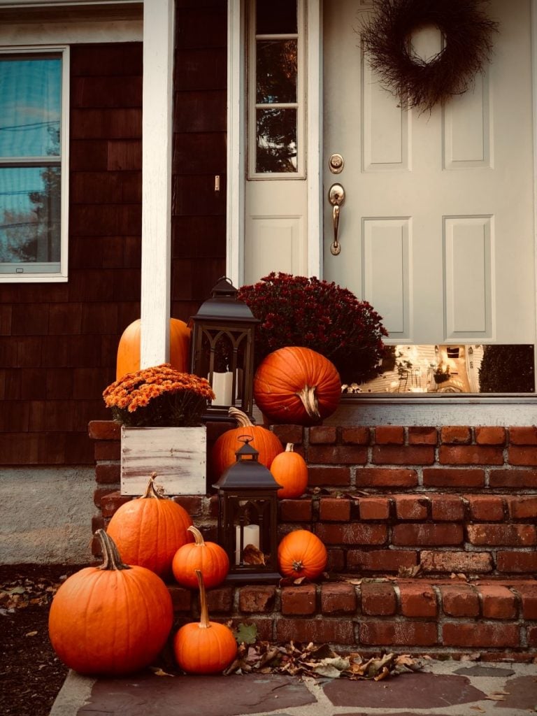 Front porch decorated with lanterns, pumpkins, and colorful mums for the fall season